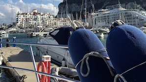 Un puerto deportivo con barcos amarrados, un flotador salvavidas y un edificio con un acantilado característico al fondo.