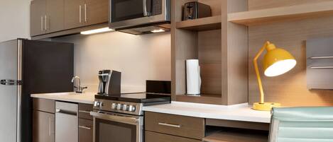 A modern kitchen with stainless steel appliances, wooden cabinets, and a yellow desk lamp.