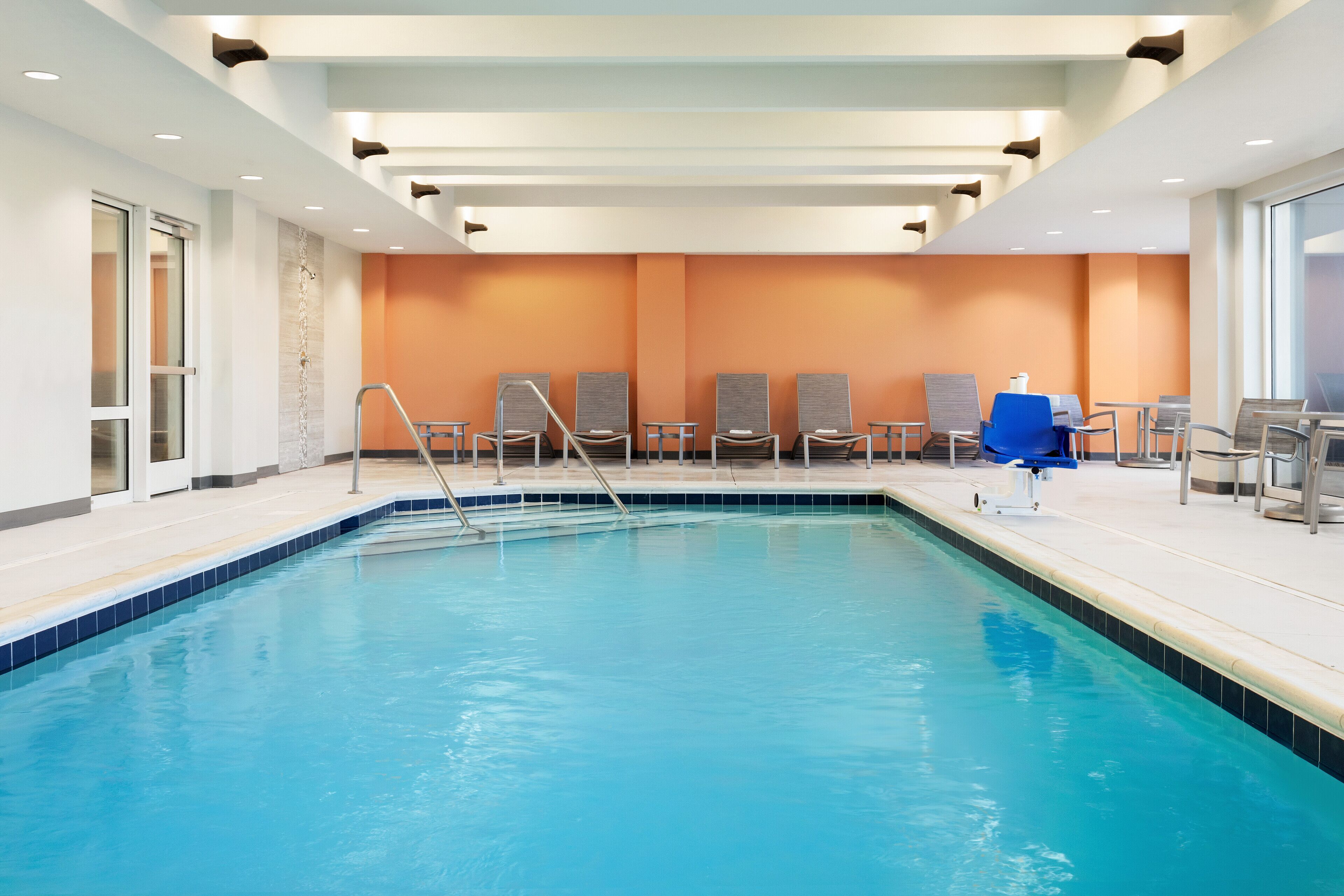 A swimming pool with a blue border, surrounded by lounge chairs and a blue umbrella.