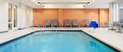 Una piscina con borde azul, rodeada de sillas de descanso y una sombrilla azul.