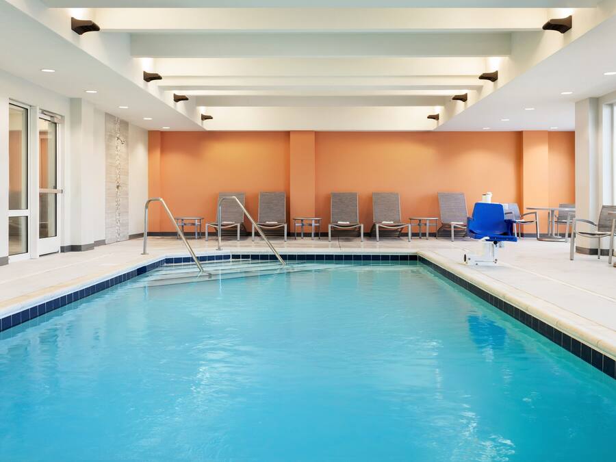 A swimming pool with a blue border, surrounded by lounge chairs and a blue umbrella.