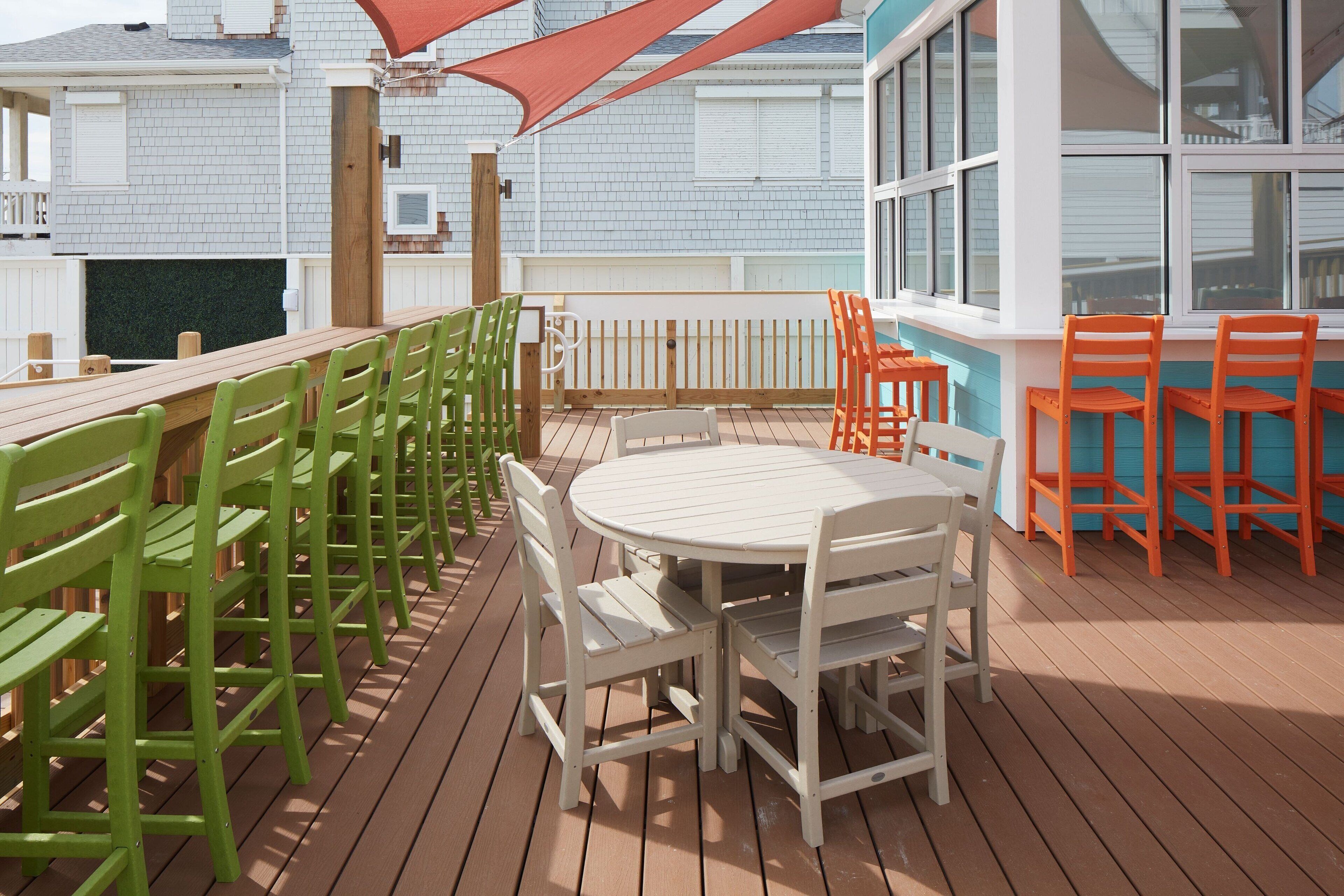 A wooden deck with a round table and chairs, surrounded by a white fence and a red canopy.