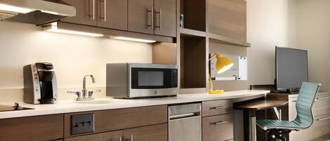 A modern kitchen with wooden cabinets, stainless steel appliances, a coffee maker, and a desk with a chair.