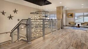 Un intérieur moderne avec un escalier en bois, un luminaire suspendu et un coin salon composé de deux fauteuils.