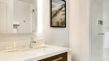 A bathroom with a white sink, a framed picture on the wall, and a glass shower enclosure.