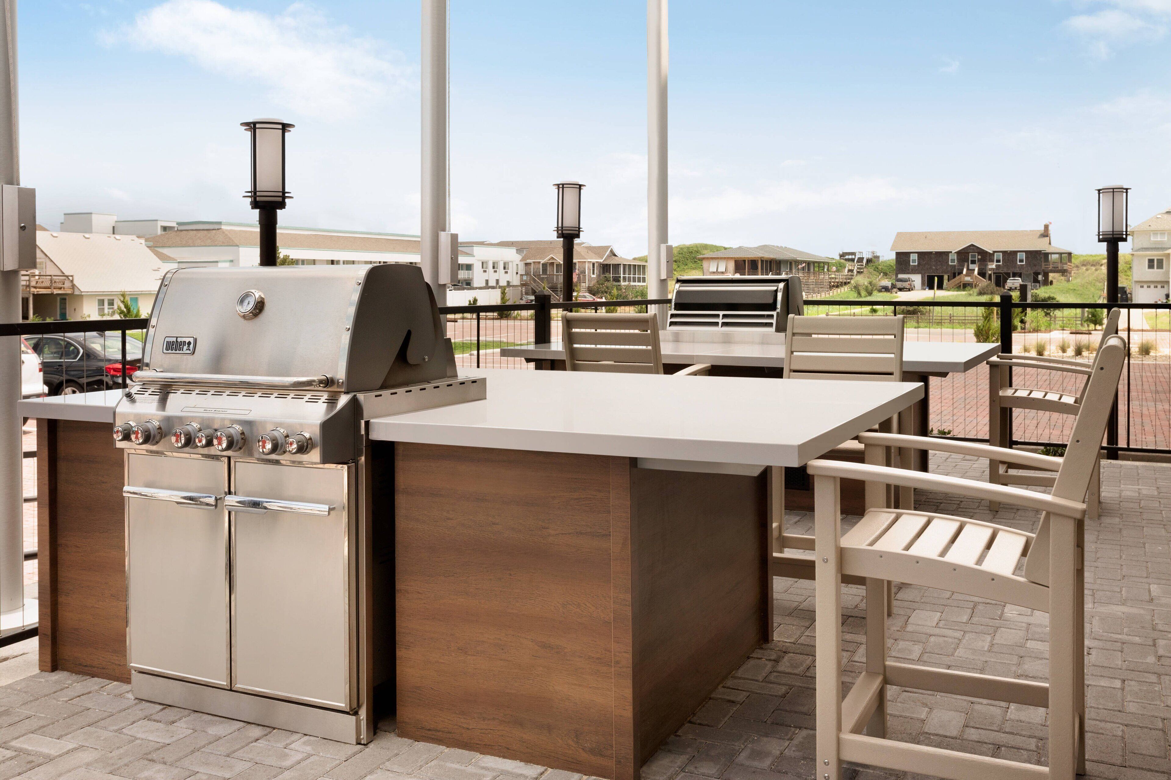 Una cocina exterior con una parrilla empotrada, una barra de madera y un área de estar con sillas.