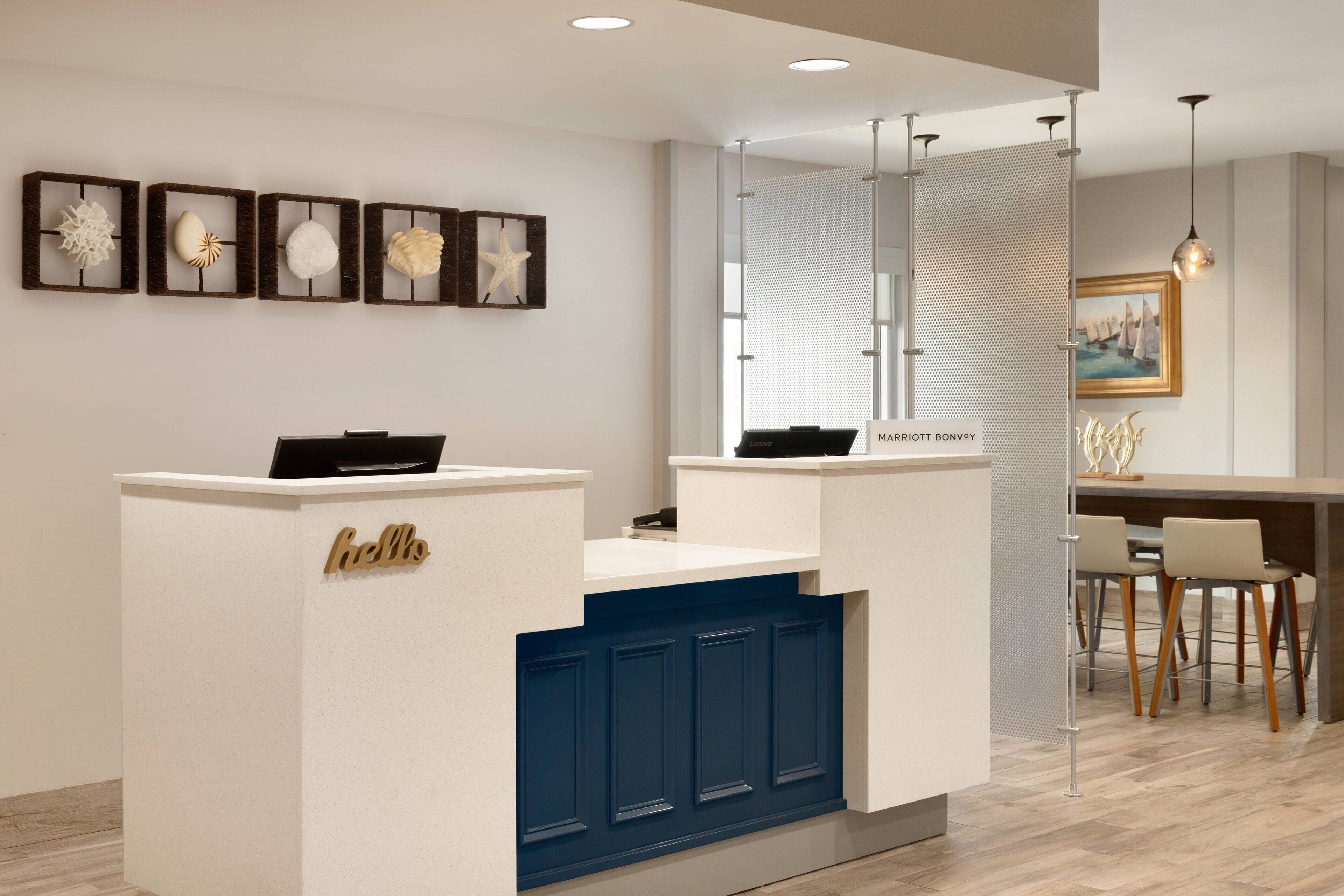 A reception desk with a 'hello' sign, a seating area with a table and chairs, and a wall with framed artwork.