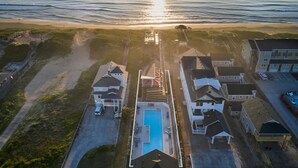 Vue aérienne d’un quartier résidentiel situé sur la côte, avec des maisons, une piscine et une plage.