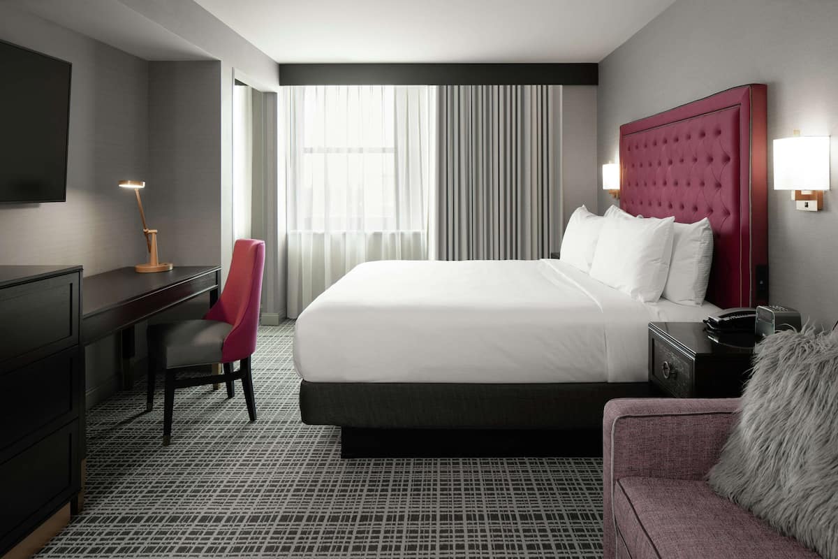 A hotel room with a large bed, a desk, a chair, and a TV.