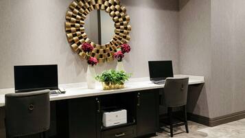 A modern reception desk with a large mirror, two chairs, a printer, and decorative flowers.