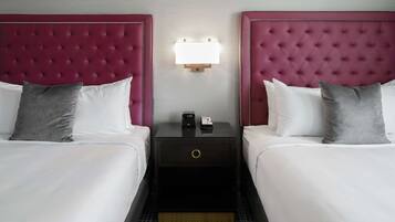 Habitación de hotel con dos camas, cada una con cabecero capitonado, mesita de noche con lámpara y un cajón pequeño.