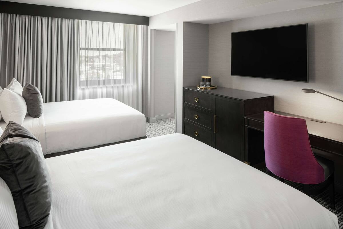 A hotel room with two beds, a desk with drawers, a flat-screen TV, and a chair.