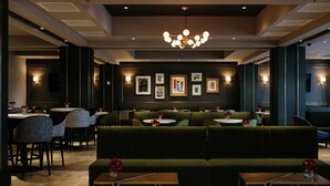 A modern dining area with green upholstered seating, round tables, and a chandelier. - The Axis Moline Hotel, Tapestry Collection by Hilton (Moline)