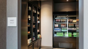 A market area with shelves stocked with various products and a refrigerated beverage dispenser. - The Axis Moline Hotel, Tapestry Collection by Hilton (Moline)