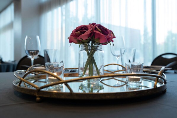A table with a glass vase containing a single rose, surrounded by candles and glasses on a tray.