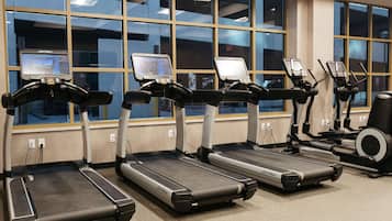 Une salle de sport équipée de tapis de course et d’appareils elliptiques, dotée de grandes fenêtres et d’écrans pour suivre les exercices.