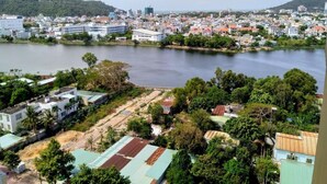 A coastal town with buildings along the waterfront, a large body of water, and a hilly background. - Hidden from the noise (Tp. Vũng Tàu)