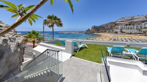 En balkon med udsigt til en strand, palmer og en klar himmel.