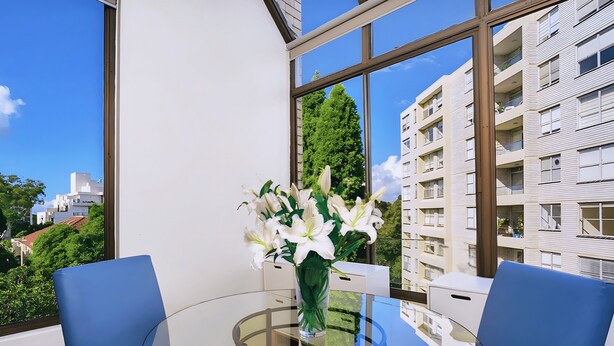 A modern room with a glass table, two blue chairs, and a vase of white flowers. - Cremorne - HAMP1 - Hampden Avenue - Bright 1BR with Sunroom, Balcony Garage Near Neutral Bay Shops (Cremorne)