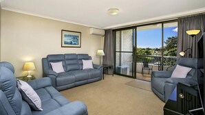 A modern living room with a grey sofa set, a small table with a lamp, and a large sliding glass door leading to a balcony. - Cremorne - HAMP1 - Hampden Avenue - Bright 1BR with Sunroom, Balcony Garage Near Neutral Bay Shops (Cremorne)