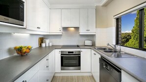 A modern kitchen with white cabinets, a built-in oven, a microwave, a toaster, and a window with a view of greenery. - Cremorne - HAMP1 - Hampden Avenue - Bright 1BR with Sunroom, Balcony Garage Near Neutral Bay Shops (Cremorne)