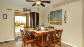 A dining area with a wooden table and chairs, a ceiling fan, a view of the outdoors, and a door leading outside. - Poolside Panorama- Perfect Lake view (Lake Havasu City)