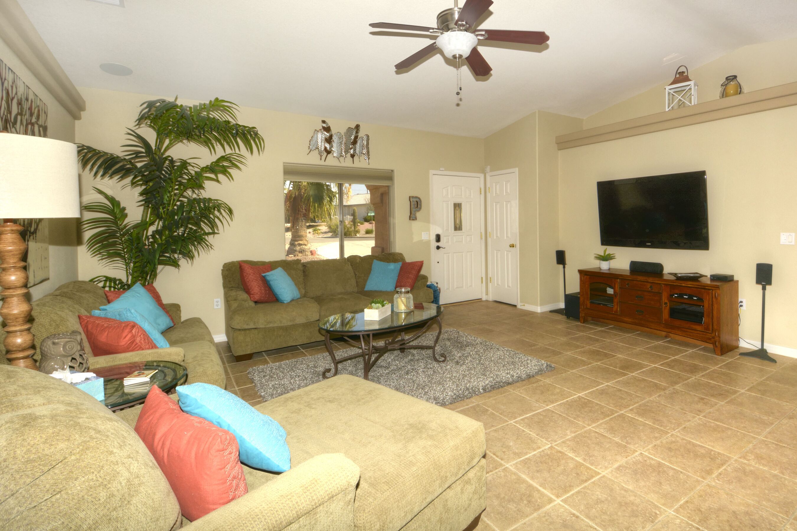 A living room with a ceiling fan, a television, a sofa set, a coffee table, and a potted plant.