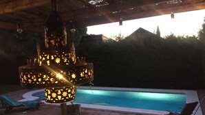 A poolside area with a decorative hanging light fixture and lounge chairs. - Comfortable apartment and swimming pool in the shade of the pine forest of Chipiona (Chipiona)