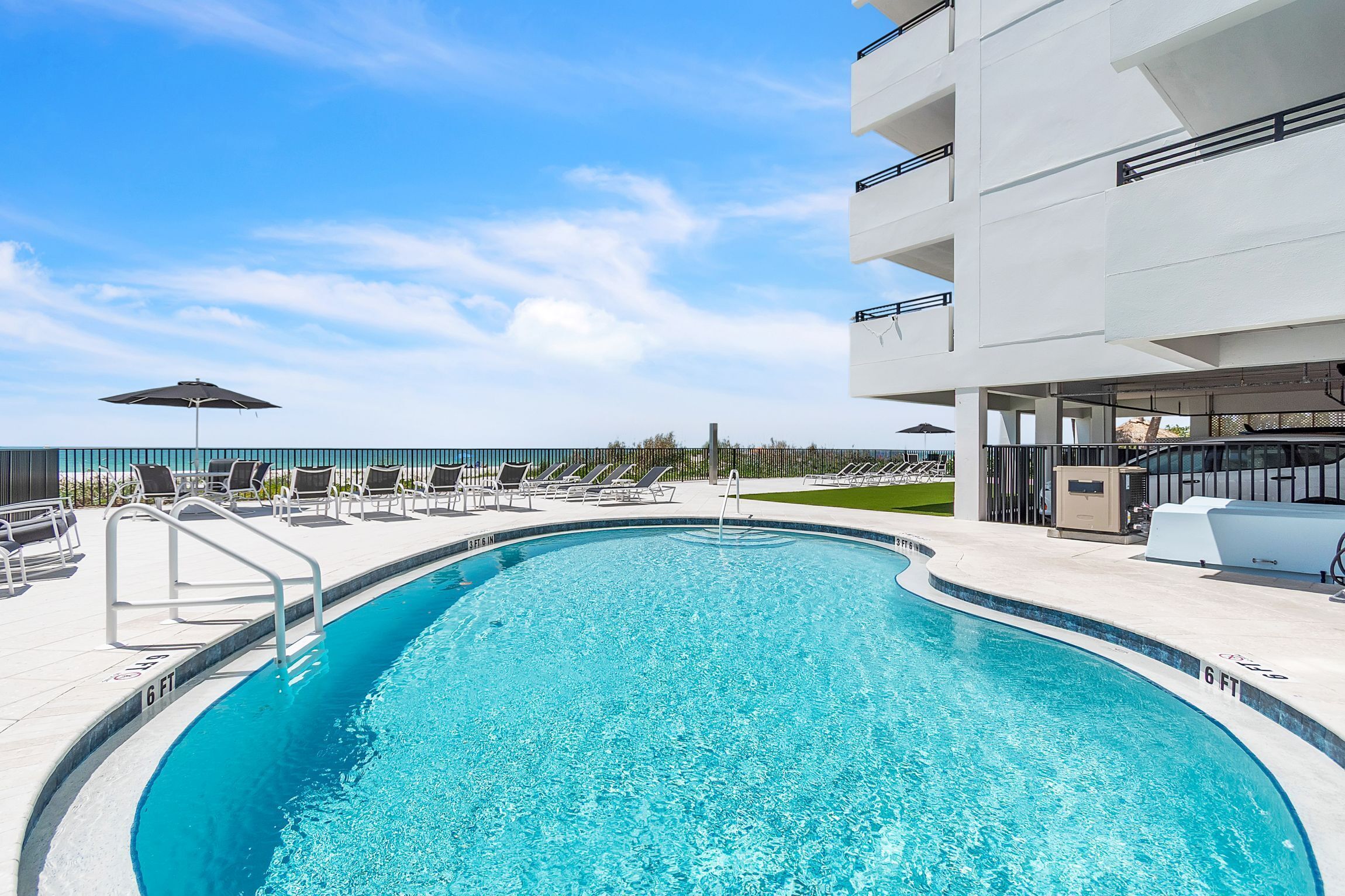 A swimming pool with lounge chairs and umbrellas, surrounded by a modern building with balconies.