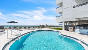 Ein Pool mit Liegestühlen und Sonnenschirmen, umgeben von einem modernen Gebäude mit Balkonen.