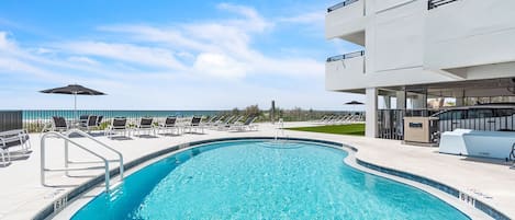 A swimming pool with lounge chairs and umbrellas, surrounded by a modern building with balconies.