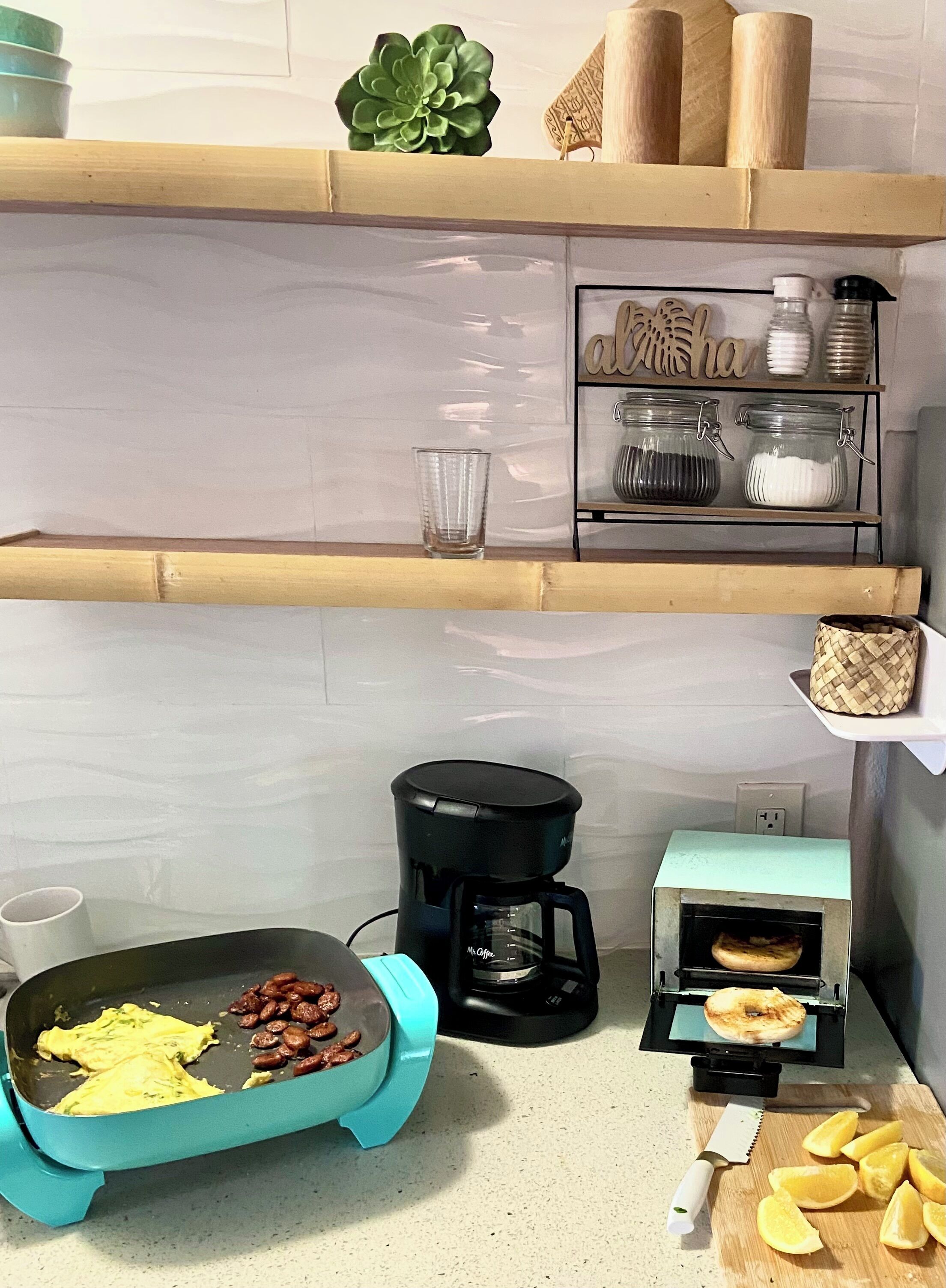 Una cocina con horno tostador, cafetera y tostador. También hay algunos alimentos en la encimera.