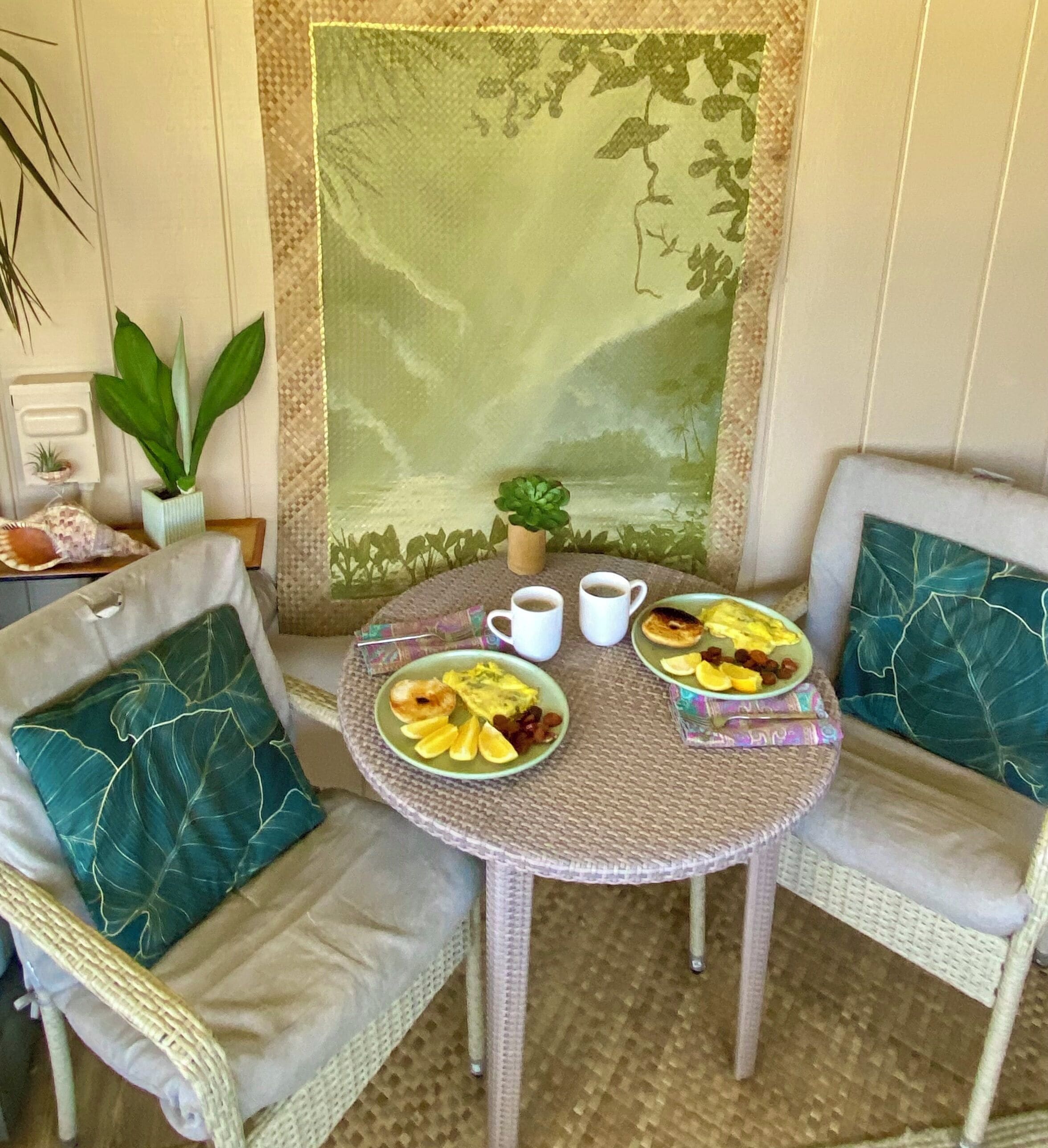 A dining area with two wicker chairs, a woven table, and a large painting of a landscape.