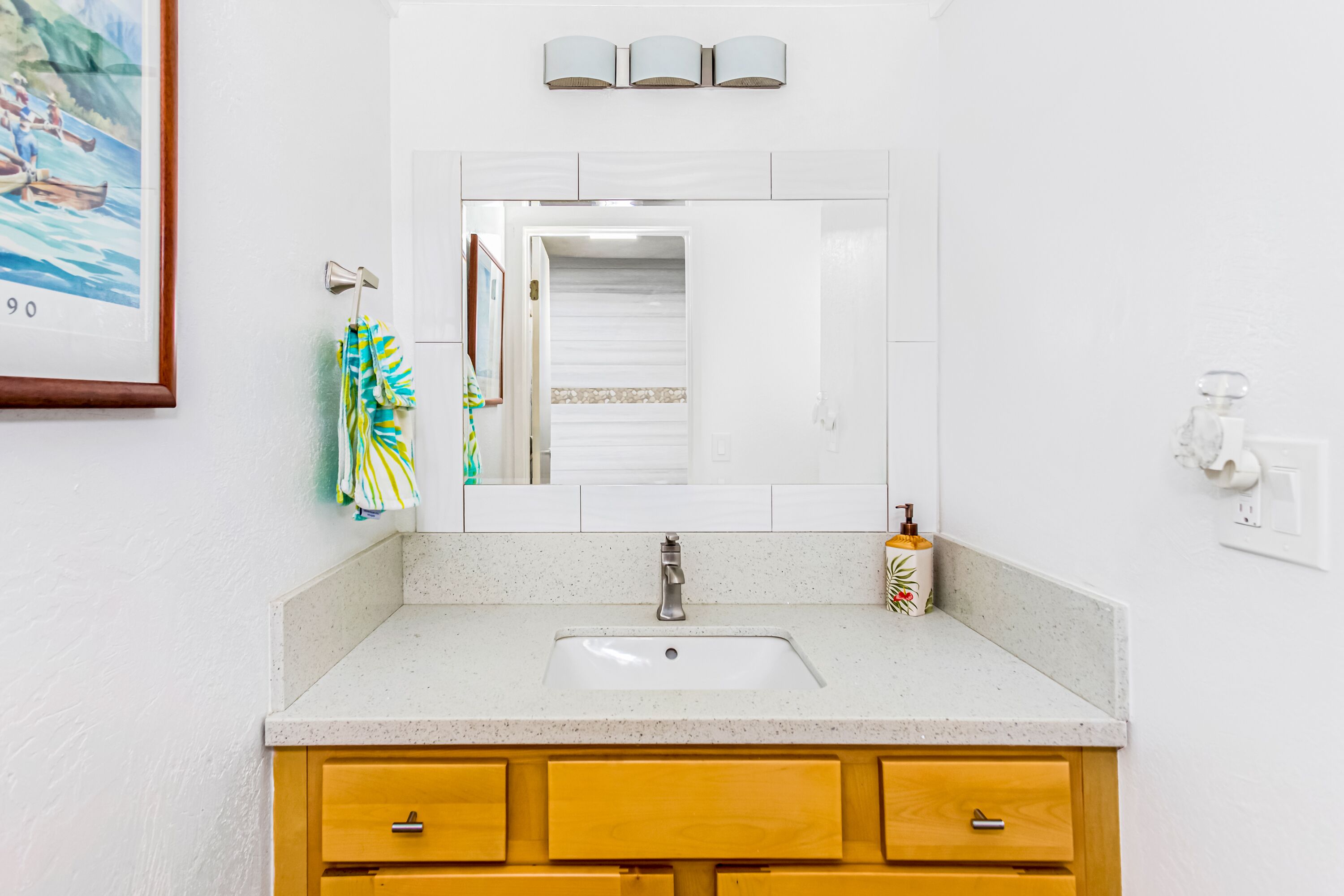 A bathroom with a white sink, wooden cabinets, a towel rack with a striped towel, and a framed picture on the wall.