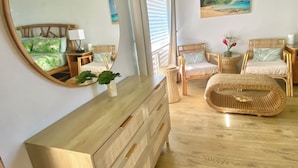 Un dormitorio con un aparador de madera, dos sillas de mimbre, un espejo grande y un cuadro de un paisaje.