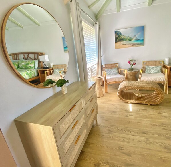 A bedroom with a wooden dresser, two wicker chairs, a large mirror, and a painting of a landscape.