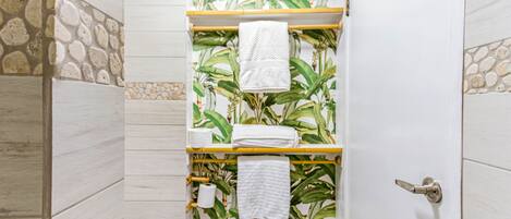 A bathroom with a shower, a toilet, and a towel rack with towels.