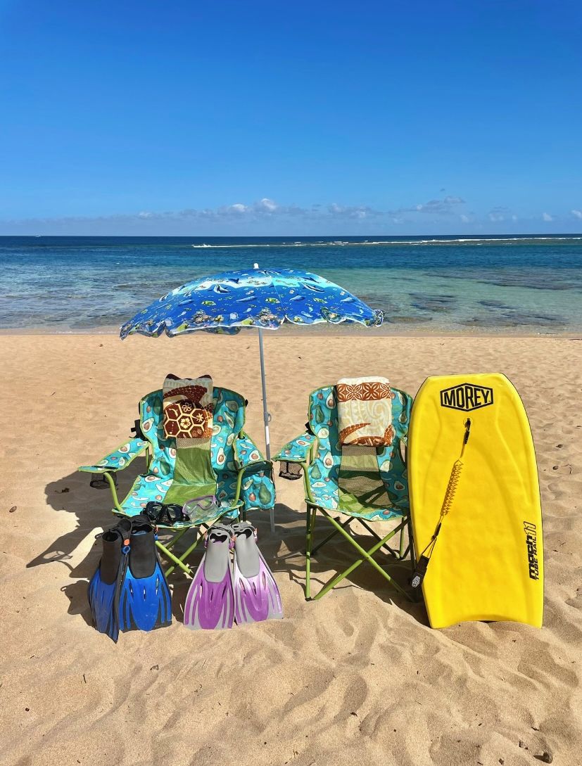 Escena de playa con una sombrilla azul, sillas de playa coloridas y una tabla de surf amarilla.