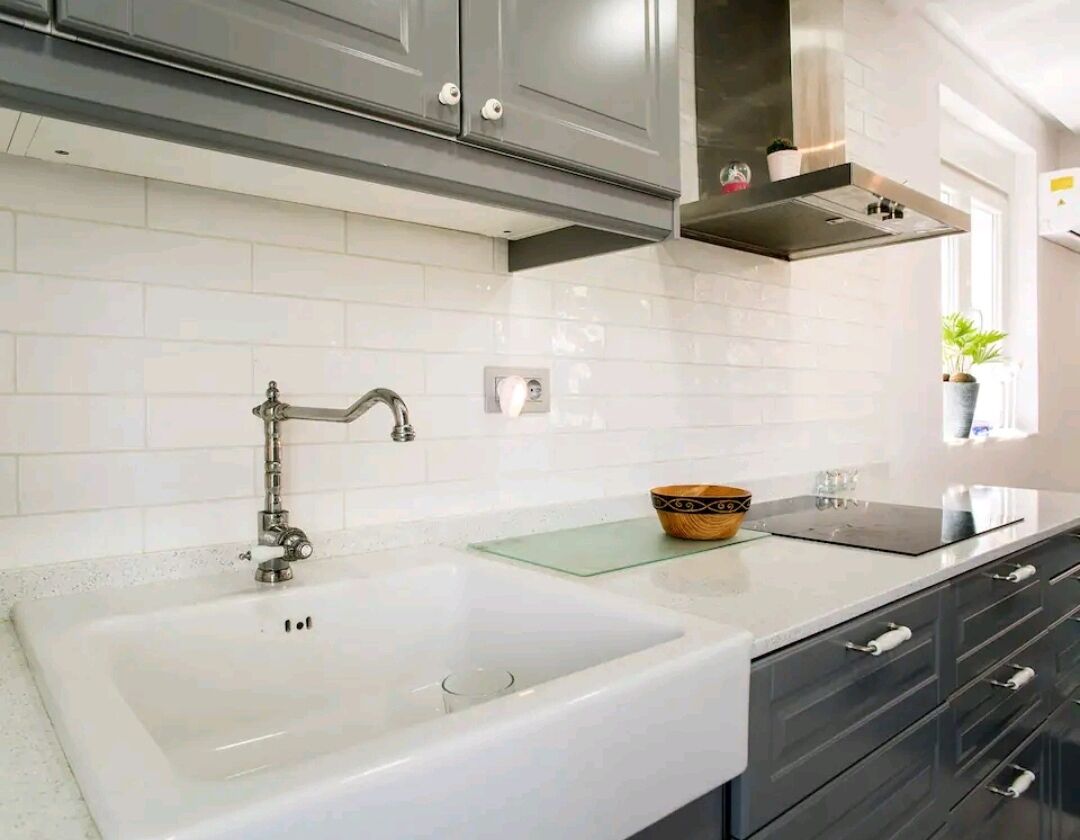 A modern kitchen with white tiles, a double sink, stainless steel cabinets, and a glass countertop.