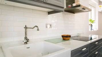 A modern kitchen with white tiles, a double sink, stainless steel cabinets, and a glass countertop.