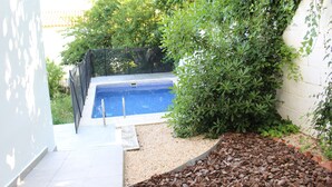 Une piscine entourée de verdure et bordée d’un mur blanc.