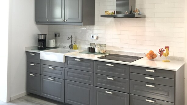 Une cuisine moderne avec des meubles gris, un plan de travail blanc et une hotte de cuisine en acier inoxydable.