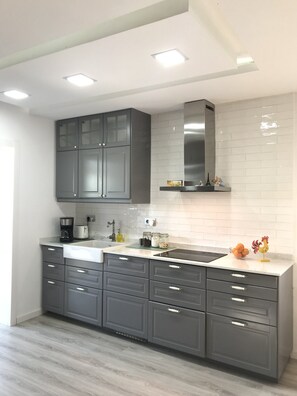 Una cucina moderna con mobili grigi, un piano di lavoro bianco e una cappa aspirante in acciaio inossidabile.