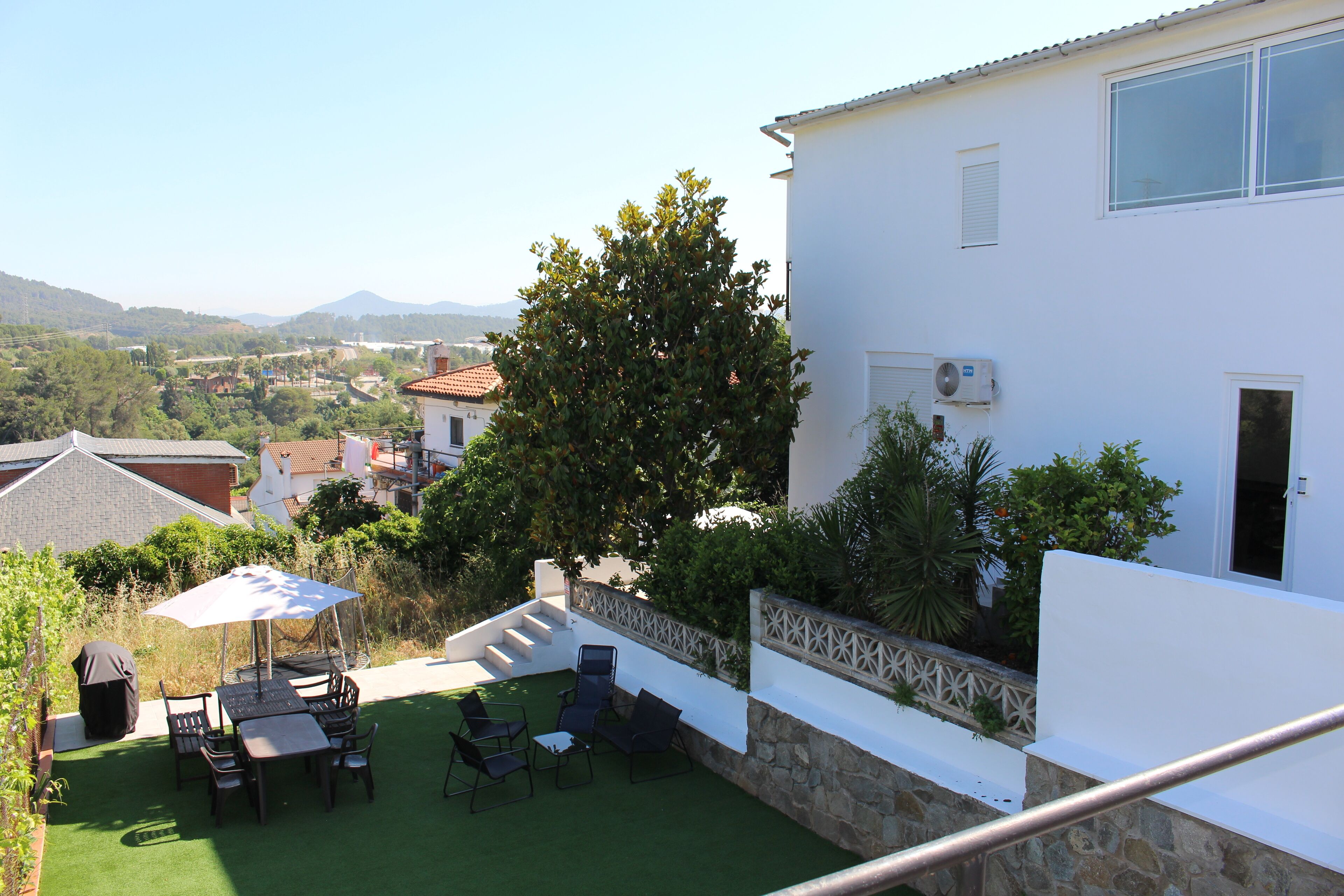 A patio with outdoor furniture and a covered table, surrounded by a white building with a stone wall and a view of the countryside.
