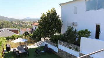 A patio with outdoor furniture and a covered table, surrounded by a white building with a stone wall and a view of the countryside.