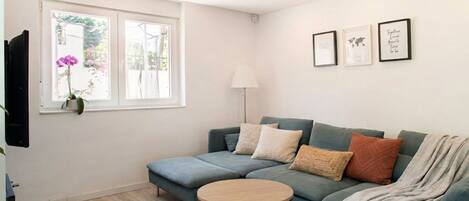 A modern living room with a sectional sofa, a round coffee table, and a large window with a view of greenery.