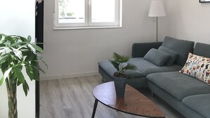Un salon moderne avec un canapé gris, une petite table ronde, une plante en pot et une lampe.