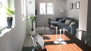 Un salon moderne avec un canapé gris, une table à manger en bois agrémentée de bougeoirs blancs et une plante en pot près de la fenêtre.