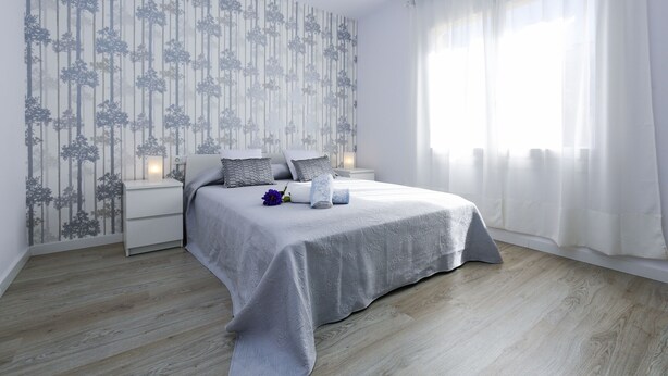 Een slaapkamer met een bed, nachtkastjes, een muur met een boommotief en een raam met gordijnen.