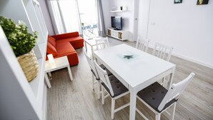 Een moderne woonkamer met een witte eettafel, een rode bank en een televisie op een wit meubel.